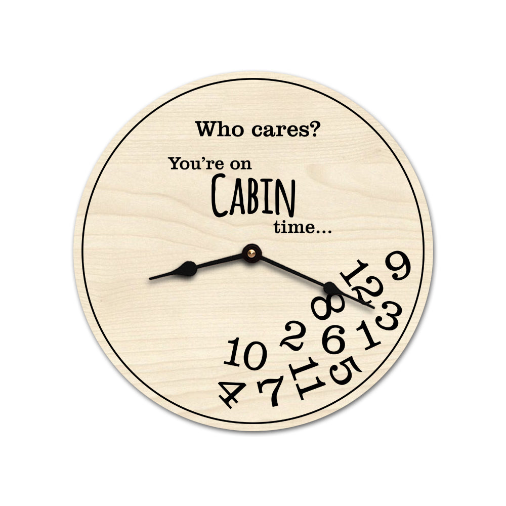 A round wooden novelty wall clock with a light natural wood finish and black printed text reading 'Who cares? You're on CABIN time.